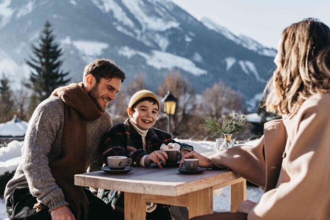 Familie sitzt draußen auf einem Tisch und trinken Heißgetränke